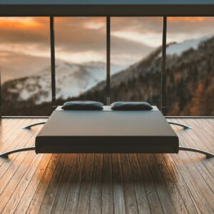Minimalist bedroom with large windows offering a breathtaking mountain view during sunset.